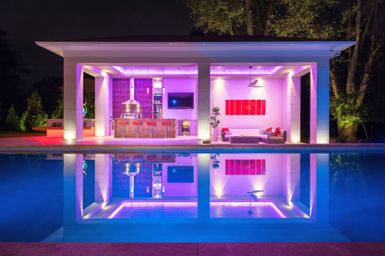 View of the outdoor kitchen from the pool at night with custom lights