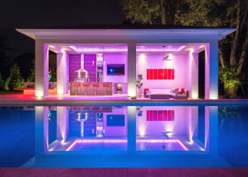 View of the outdoor kitchen from the pool at night with custom lights