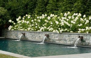 Stone wall over pool with waterfalls and flowers for Luxury Landscaping in Great Falls, VA